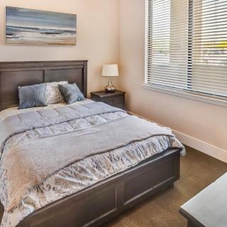 A cozy bedroom with a neatly made bed and a bedside lamp near a window.