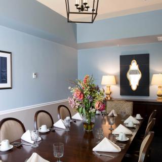 A neatly arranged dining room with a table set for eight, featuring a floral centerpiece and blue walls.