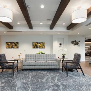 A modern living room featuring a grey sofa, armchairs, and decorative lighting under wooden ceiling beams.