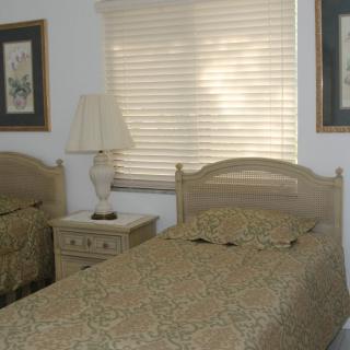 A cozy bedroom featuring twin beds with matching bedding, a central nightstand with a lamp, and framed art on the walls.