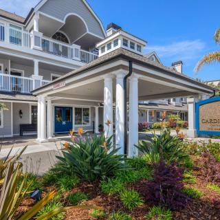 A charming hotel building with elegant architecture surrounded by lush greenery on a sunny day.