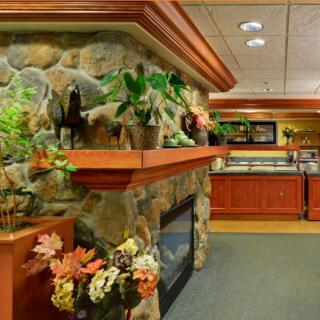 A cozy lobby interior featuring a decorated stone fireplace with plants and flowers, leading to a wooden counter area.