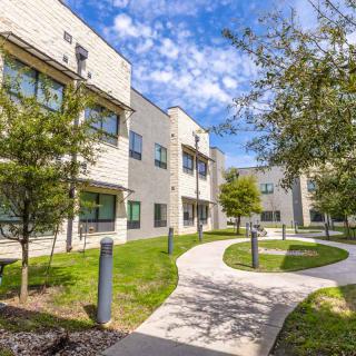 A sunny view of a residential apartment complex with a pathway and green landscaping.