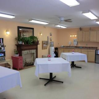 A cozy dining area featuring white tablecloths on tables and a welcoming kitchen backdrop.