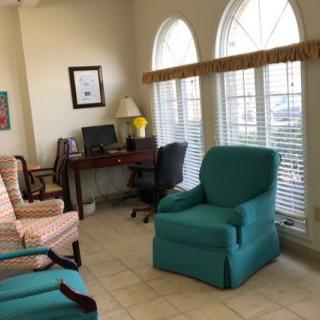 A cozy living room with colorful chairs and a computer desk by the windows.