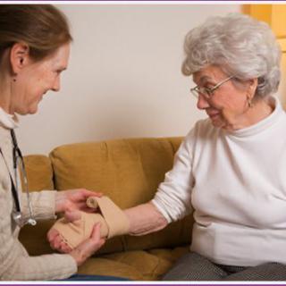 A nurse assists an elderly woman with a bandaged hand at home.