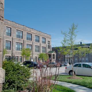 A view of a residential building with parked cars along a street lined with trees.
