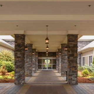 A covered entrance with stone pillars leading to a building, surrounded by landscaped greenery.