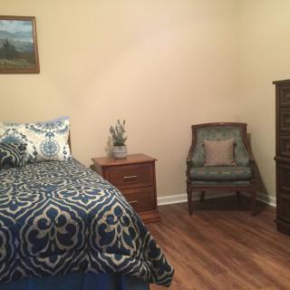 A cozy bedroom with a bed, nightstand, chair, and dresser.