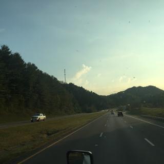 A scenic view of a highway surrounded by mountains and trees during sunset.