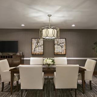 A modern dining room with elegant decor, featuring a central chandelier, a wooden dining table surrounded by upholstered chairs, and decorative wall art.