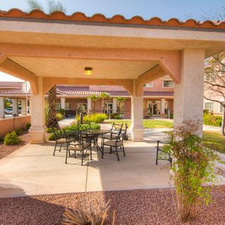 A sunny outdoor patio area with furniture and a gazebo surrounded by a garden.