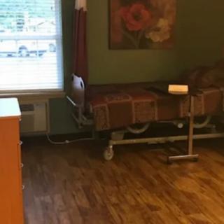 A hospital room with a bed, window, and artwork on the wall.