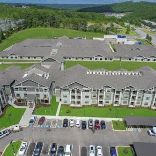 Aerial view of a modern apartment complex surrounded by green spaces and parking areas.