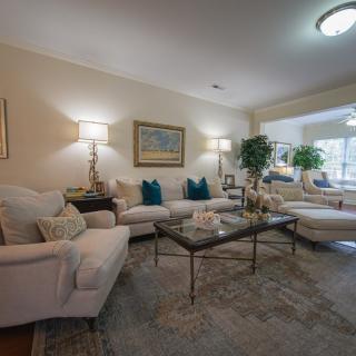 A cozy living room featuring plush sofas, a glass coffee table, decorative pillows, and ambient lighting.