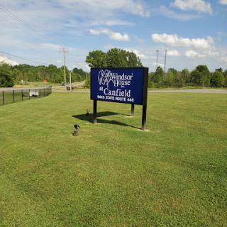 A large blue sign stands in a grassy field under a partly cloudy sky.