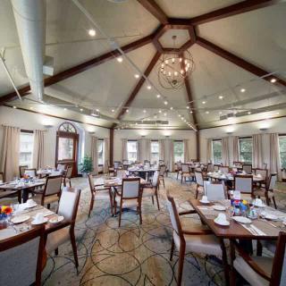 An elegant dining room with neatly arranged tables and a central chandelier.
