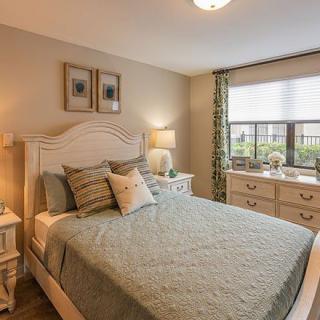 A cozy bedroom interior featuring a neatly made bed, bedside tables with lamps, and a window with patterned curtains.