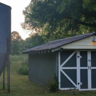 A small barn next to a silo in a rural setting during sunset.