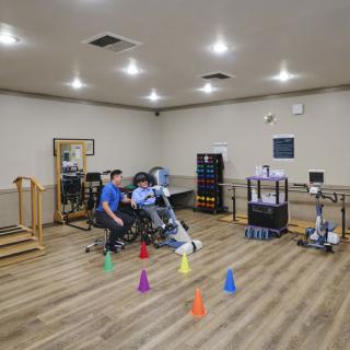 A physical therapy session with a therapist assisting a person on exercise equipment in a rehabilitation gym.