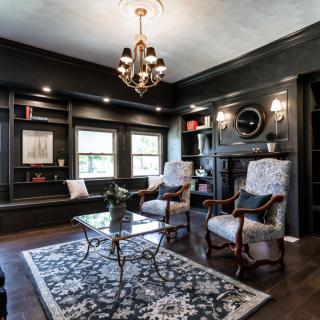 A traditional living room with dark walls, featuring elegant armchairs, a rug, and a chandelier.