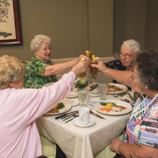 A group of elderly friends enjoying a meal and toasting at a dining table.