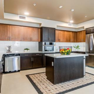 A modern kitchen with wooden cabinets and a central island, featuring stainless steel appliances and a fruit bowl.