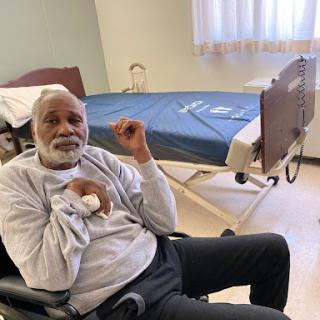 An elderly man sitting in a wheelchair in a hospital room.