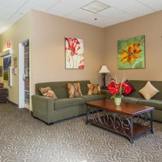 A cozy living room with green couches, a wooden coffee table, and colorful artwork on the walls.