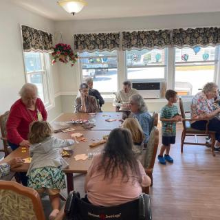 A group of seniors and children are gathered indoors, socializing and playing cards together.