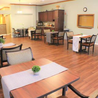 A cozy dining area with wooden floors, tables, and chairs, decorated with small plants.