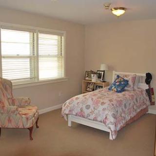 A cozy bedroom with a single bed, floral bedding, an armchair, and natural light from the window.