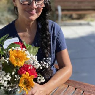 A woman with glasses and a braid, holding a bouquet of colorful flowers outside.