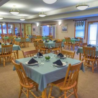 A well-arranged dining room with tables covered in blue tablecloths, set with plates and black napkins.