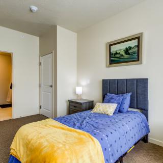 A cozy bedroom with a single bed featuring blue bedding and a yellow blanket, complemented by a nightstand and lamp, all set on a carpeted floor.