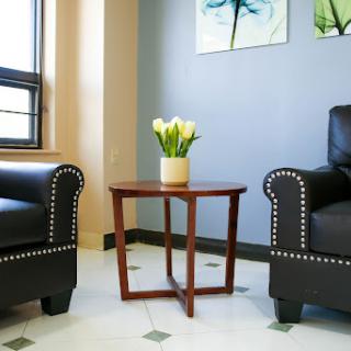 A cozy seating area featuring two black chairs, a small wooden table, and a vase of flowers.