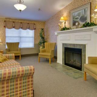 A cozy living room with a fireplace surrounded by armchairs and a patterned sofa, featuring traditional decor.
