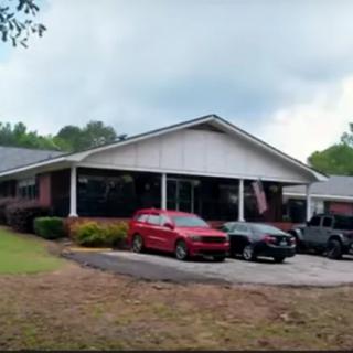 A residential building with several cars parked in the driveway under a cloudy sky.