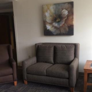 A cozy living room setup featuring a loveseat and armchair, complemented by a floral painting.