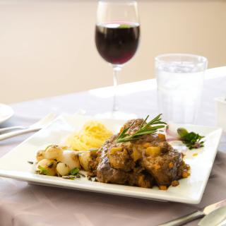 A plated meal featuring meat, potatoes, and vegetables, accompanied by a glass of red wine on a dining table.