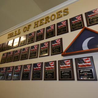 A wall adorned with plaques under the title 'Wall of Heroes,' featuring American flags and a folded triangular flag, honoring military service.