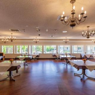 A spacious dining room with chandeliers, several tables, large windows, and a wooden floor.
