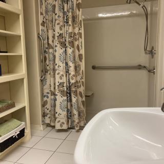 A cozy bathroom with a floral shower curtain, shelving, and neatly organized towels.