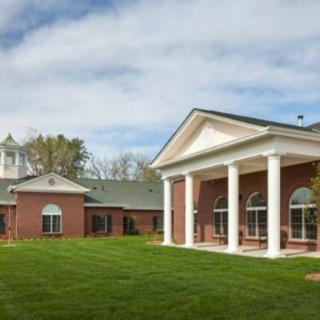 A brick building with white columns and a well-manicured lawn under a partly cloudy sky.