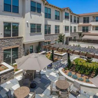 A modern apartment complex featuring a landscaped courtyard with outdoor seating and patio umbrellas.
