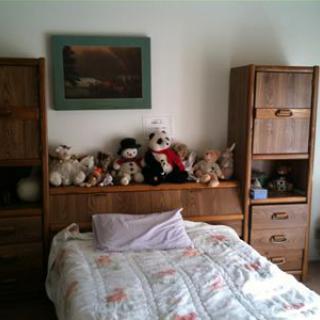 A cozy bedroom with a bed adorned with stuffed animals and surrounded by wooden shelves.