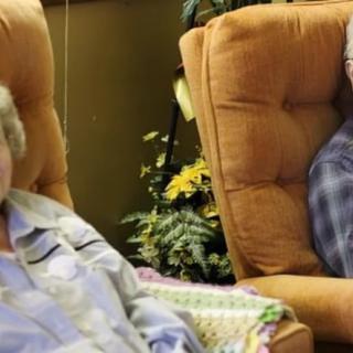 An elderly couple sitting comfortably in cozy chairs, enjoying a relaxed moment at home.