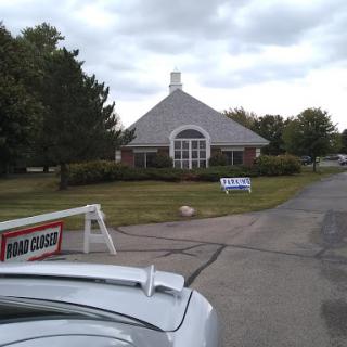 A view of a building with a cloudy sky overhead, featuring nearby trees and signs for parking.