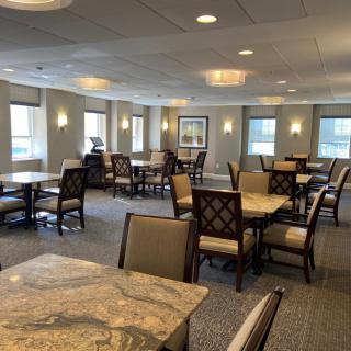 A spacious dining area with multiple tables and chairs, featuring large windows and warm lighting.