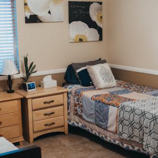 A cozy and well-decorated bedroom with a bed, nightstand, and floral artwork.